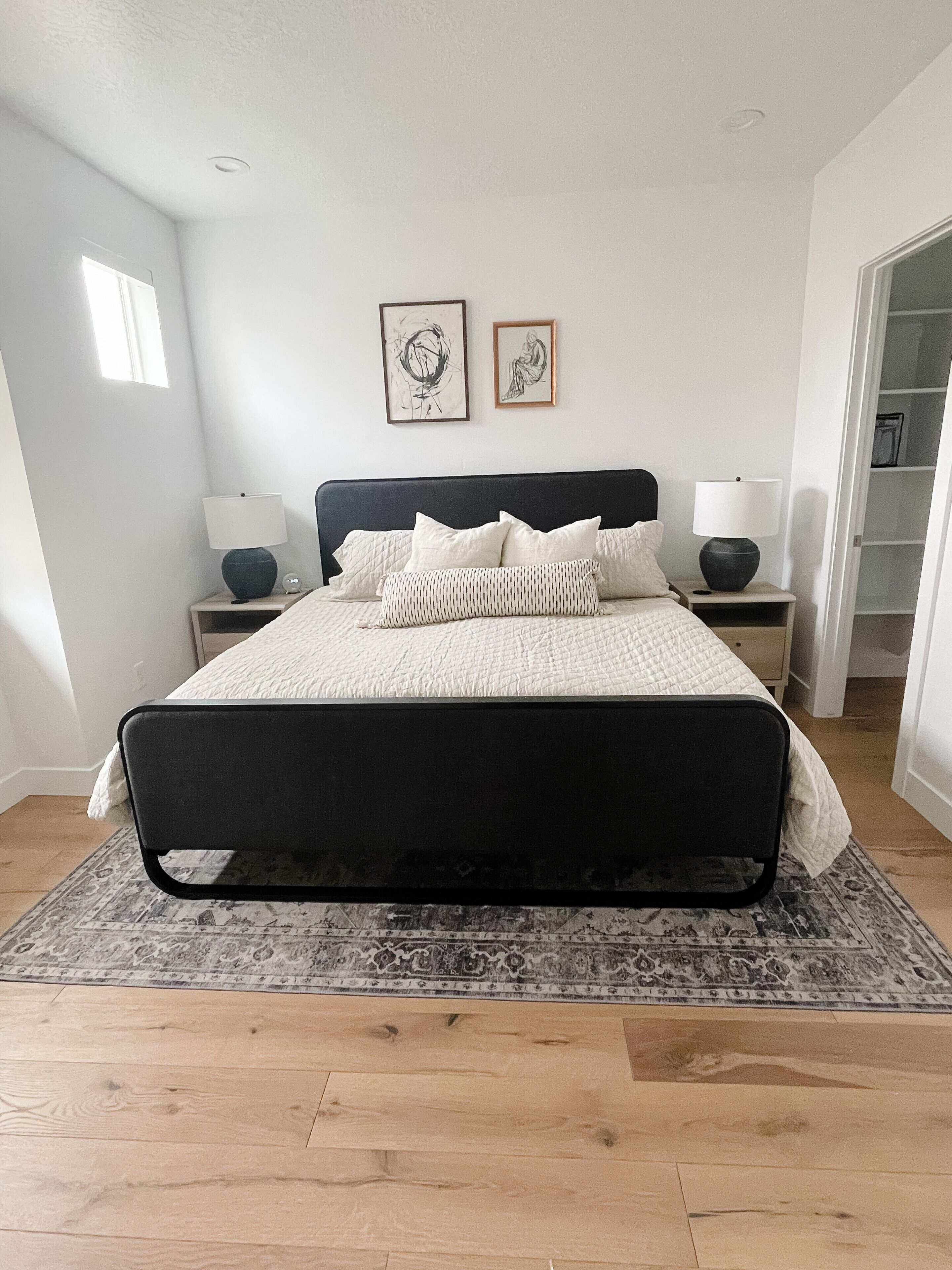 A modern bedroom with a large bed, two bedside tables with lamps, a patterned rug, and artwork on the wall.