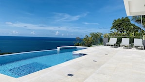 Une piscine offrant une vue dégagée sur l’océan, entourée d’une terrasse carrelée et de chaises longues.