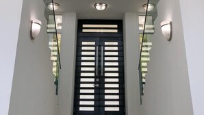 Un escalier moderne avec une rampe en verre, une porte noire à lattes horizontales et un éclairage encastré.