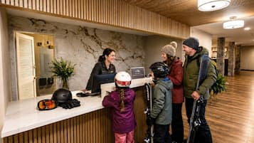 A reception desk with a receptionist, a child with a helmet, and two adults with ski gear.