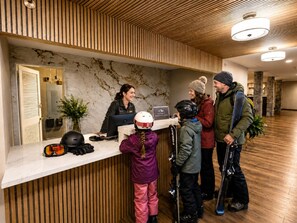 A reception desk with a receptionist, a child with a helmet, and two adults with ski gear.