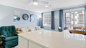 A modern living room with a large island table, a green armchair, a beige sofa, and a view of the building outside. - ML204 Chairlift View Near Village WiFi EZ Parking (Dunmore)