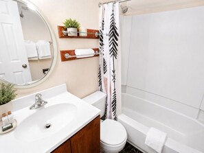 Un baño con lavamanos blanco, armario de madera, espejo y cortina de ducha estampada con hojas.