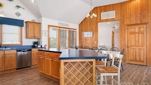 A kitchen with wooden cabinets, a central island with a wine rack, and a dining area with chairs. - Oceanfront, Pet- & Handicap- Friendly Home w/ Heated Pool, Elevator & Game Room (Salvo)
