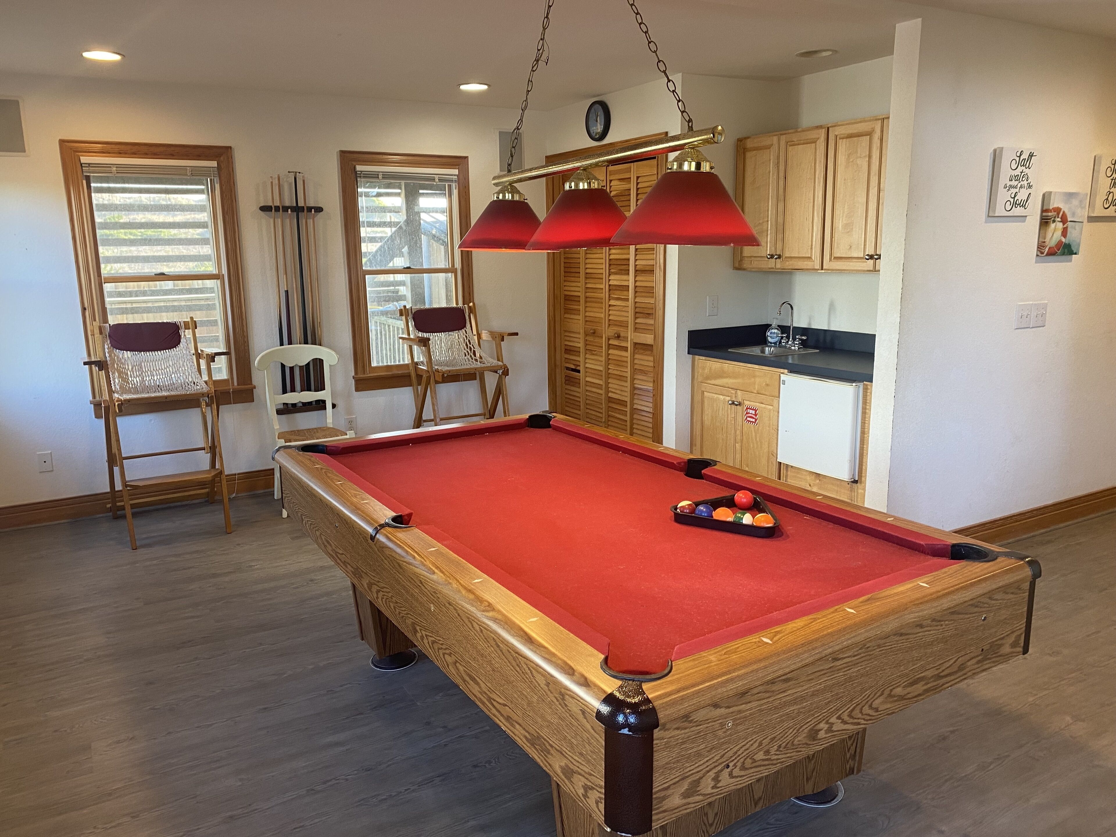 Une table de billard recouverte d’un feutre rouge, dotée de caissons en bois et comprenant un petit coin cuisine avec un évier.