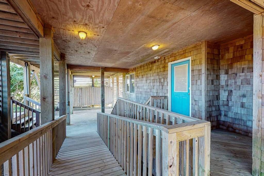 A wooden deck with a railing, a door with a blue frame, and a wooden ceiling with recessed lighting.