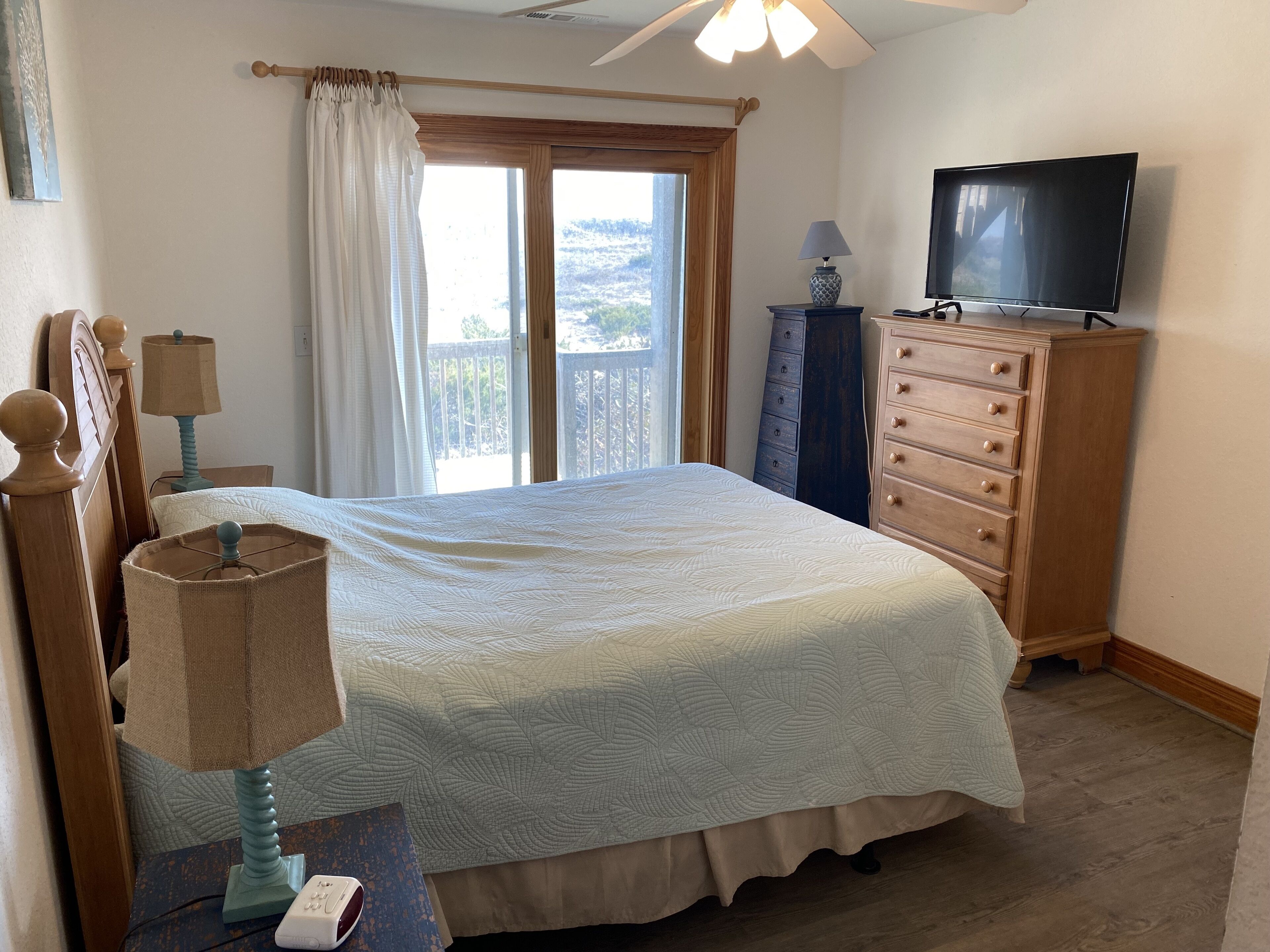Une chambre à coucher avec un lit, une commode, un téléviseur et une fenêtre avec des rideaux.