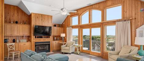 A spacious living room with a fireplace, wooden walls, a large TV, and a balcony with a view.