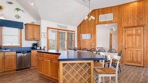 Una cocina con armarios de madera, una isla central con un espacio para vinos y una zona de comedor con sillas.