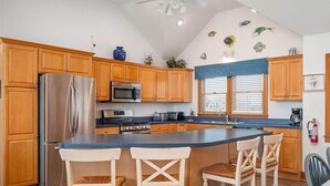 Cocina con armarios de madera, electrodomésticos de acero inoxidable, una isla central con taburetes y decoración de peces en la pared.