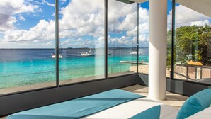Une chambre moderne dotée de grandes fenêtres donnant sur une marina et sur des eaux turquoise.