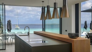 Une cuisine moderne dotée d’un grand îlot central, offrant une vue sur l’océan, et d’un coin repas avec des chaises et des parasols.
