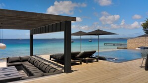 Une terrasse en bois avec des chaises longues et une piscine donnant sur la mer.