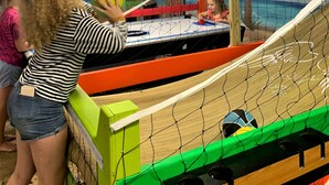 A volleyball game in a netted area with a tropical mural in the background. - Medley Manor Weekday Special! (East Peoria)