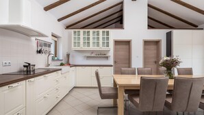 A modern kitchen with white cabinets, a wooden dining table, and a lofted ceiling with exposed beams. - Stunning home in Gostinjac (Gostinjac)