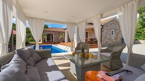 A covered outdoor seating area with a pool, wicker furniture, and a guitar. - Stunning home in Gostinjac (Gostinjac)