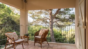 A balcony with wicker chairs and a small table, overlooking a lush green landscape.