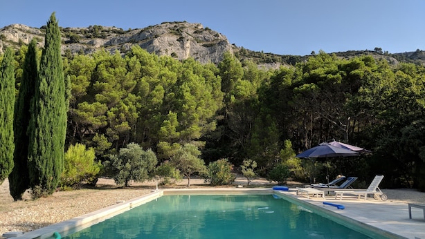 A swimming pool with lounge chairs and umbrellas, surrounded by trees and a mountainous backdrop.