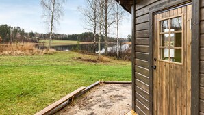 A wooden cabin with a door and window, a grassy yard, and a lake in the background. - Stunning home in Svanskog with sauna (Svanskog)