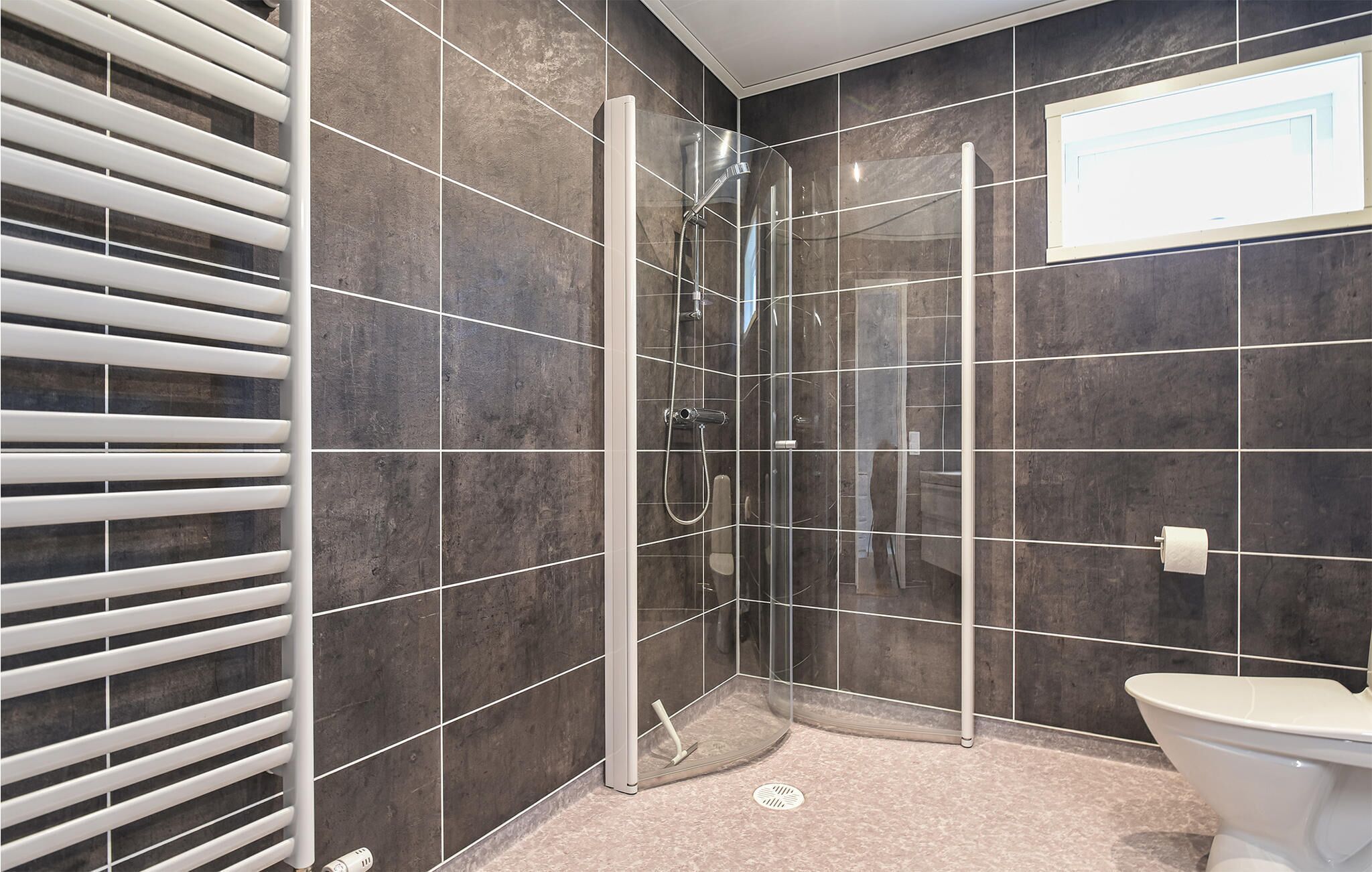 Un baño moderno con cabina de ducha de vidrio, paredes de azulejos oscuros y un inodoro.