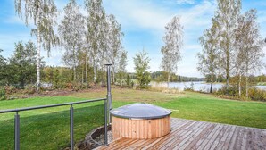 A hot tub on a wooden deck with a metal railing, surrounded by a grassy area and trees. - Stunning home in Svanskog with sauna (Svanskog)