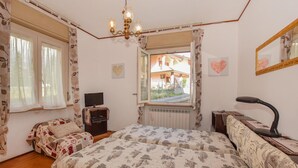 A bedroom with a bed, a desk with a chair, a television, a radiator, and a window with a view of a house. - 2 bedroom lovely apartment in Chatillon (Chatillon)
