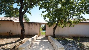 A stone pathway leading to a gate with a metal fence, surrounded by trees and a building with a tiled roof. - Amazing home in Mejannes le Clap with swimming pool (Mejannes le Clap)