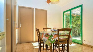 A dining area with a table set for two, wooden chairs, a patterned tablecloth, and a view through a green-framed window. - Amazing home in Mejannes le Clap with swimming pool (Mejannes le Clap)