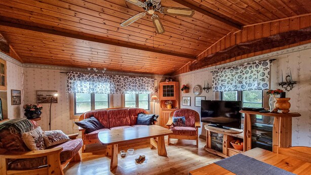 Un interior acogedor de madera con un sofá, sillas, un televisor y una mesa de comedor.