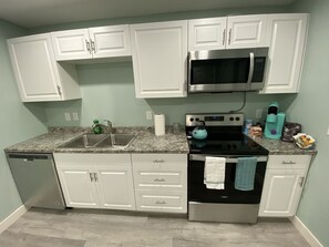 Une cuisine moderne avec des meubles blancs, un four à micro-ondes en acier inoxydable, une cuisinière noire et une bouilloire turquoise.