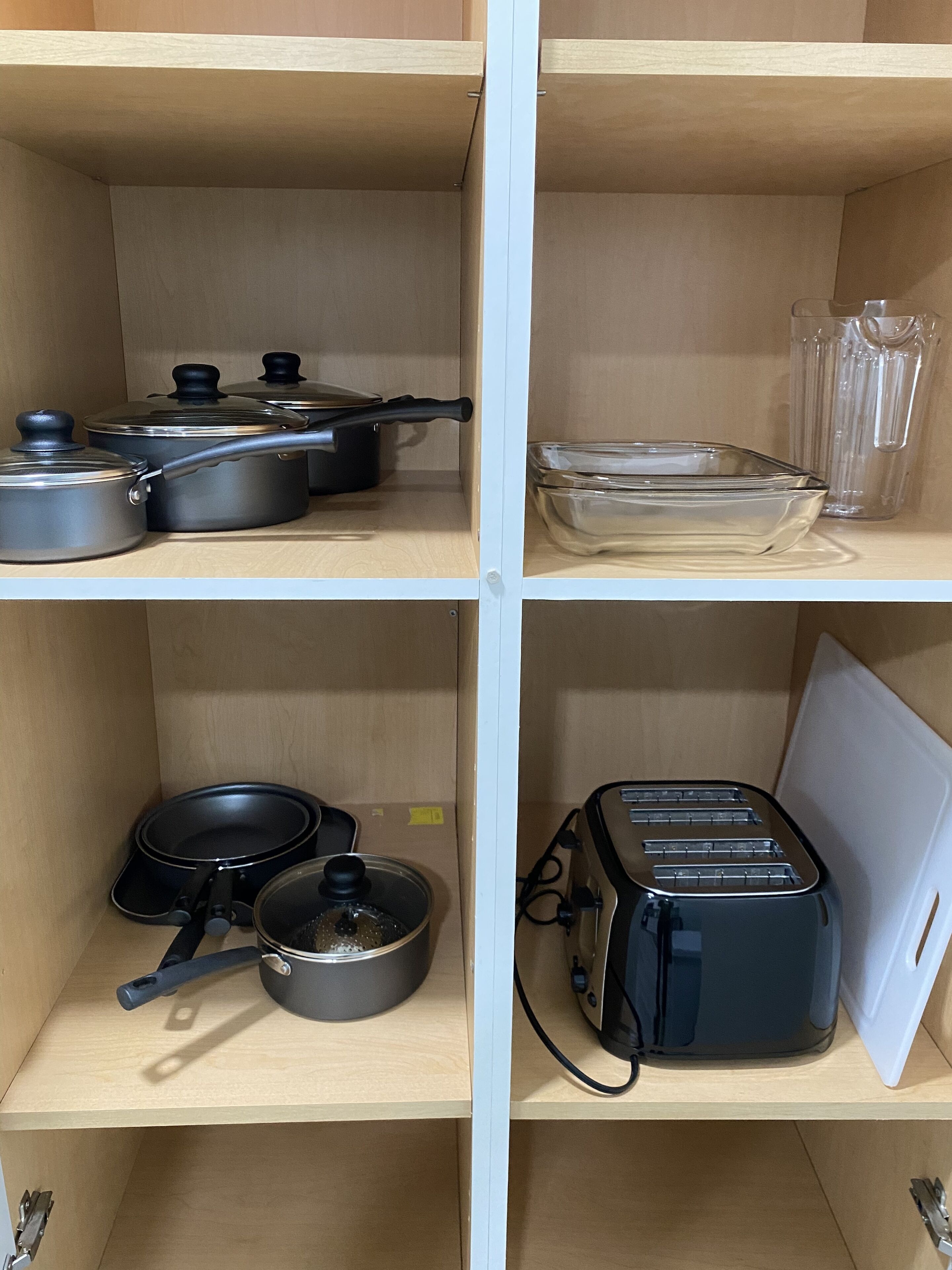 Eine Küche mit vier Holzböden, auf denen verschiedene Küchenutensilien liegen: Töpfe, Pfannen, eine Glasbowl und ein Toaster.