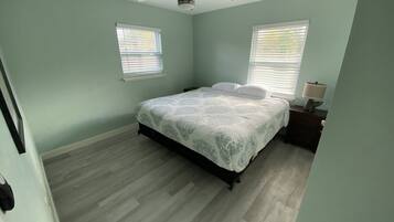 A bedroom with a bed, two windows with blinds, a ceiling fan, and a nightstand with a lamp.