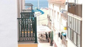 Una calle estrecha flanqueada por edificios, un balcón con barandilla metálica y vista al mar al fondo.