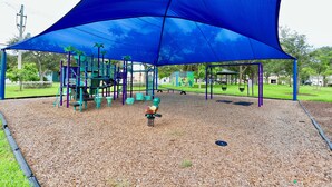 Un parque infantil con toldo azul, estructuras de juego y columpios.