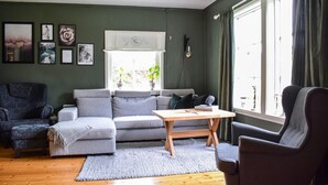 A living room with a grey sofa, a wooden coffee table, and a dark armchair. There are framed pictures on the wall and a window with curtains. - 2 bedroom cozy home in Tysse (Tysse)