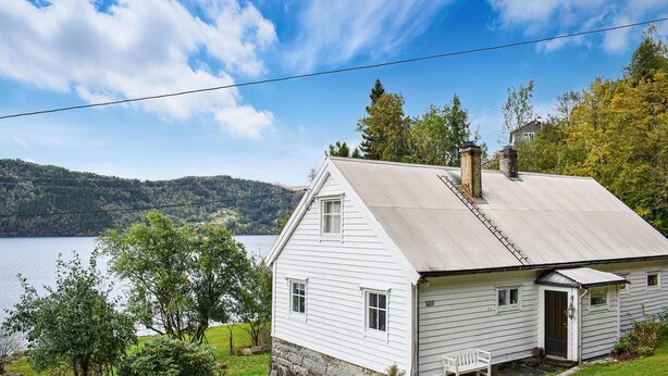 A white house with a gabled roof, a chimney, and a small porch with a bench. - 2 bedroom cozy home in Tysse (Tysse)