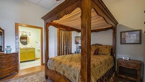 Un lit à baldaquin avec une couvre-lit à motifs floraux, une commode en bois, une petite table de chevet et un tapis.