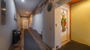 Un couloir doté d’un plancher en bois, une porte blanche ornée de motifs colorés, et une petite table sur laquelle se trouvent un sac et une boîte.