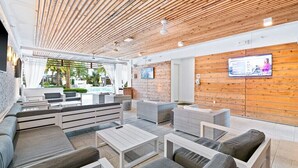 Un espace de détente extérieur moderne, doté d’un plafond en bois, de sièges confortables et d’un écran de télévision fixé au mur.