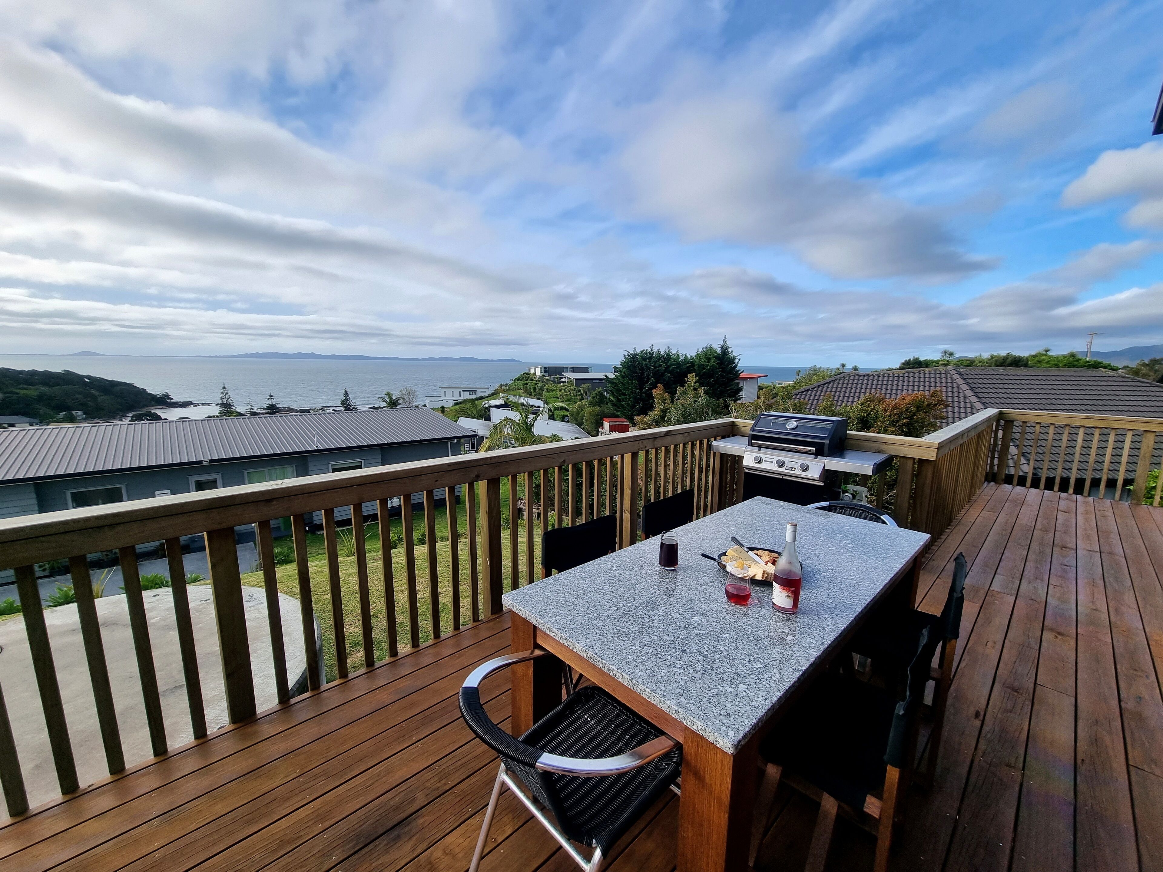 A deck with a table, chairs, and a grill overlooking a body of water.