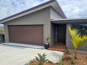 Une maison moderne à deux étages, dotée d’un garage, d’une porte d’entrée et d’un petit porche.