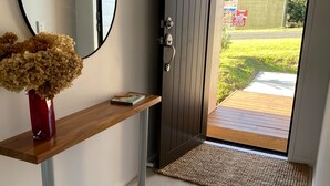 A hallway with a wooden console table, a mirror, and a door leading to an outdoor area. - Belvedere Amazing views   (Cable Bay)