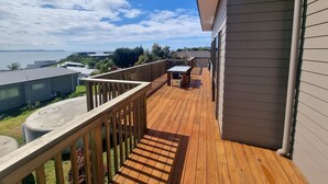 A wooden deck with a table and chairs, overlooking a body of water and a hilly landscape. - Belvedere Amazing views   (Cable Bay)