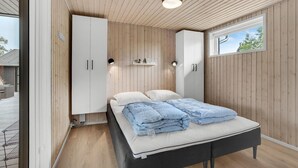 A bedroom with a bed, white wardrobe, wooden panel walls, and a window with a view. - Lovely home in Haderslev (Haderslev)