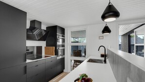 A modern kitchen with dark cabinetry, a white countertop, and a wooden cutting board with vegetables. - Lovely home in Haderslev (Haderslev)