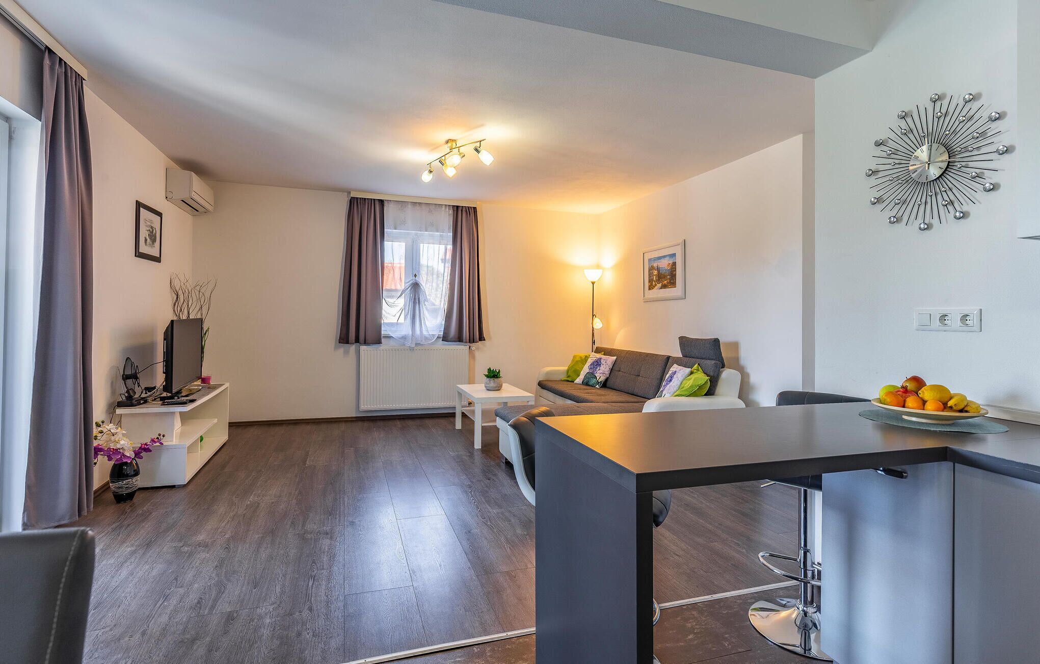 A modern living room with a sofa, a dining table, and a kitchen area with a fruit bowl.