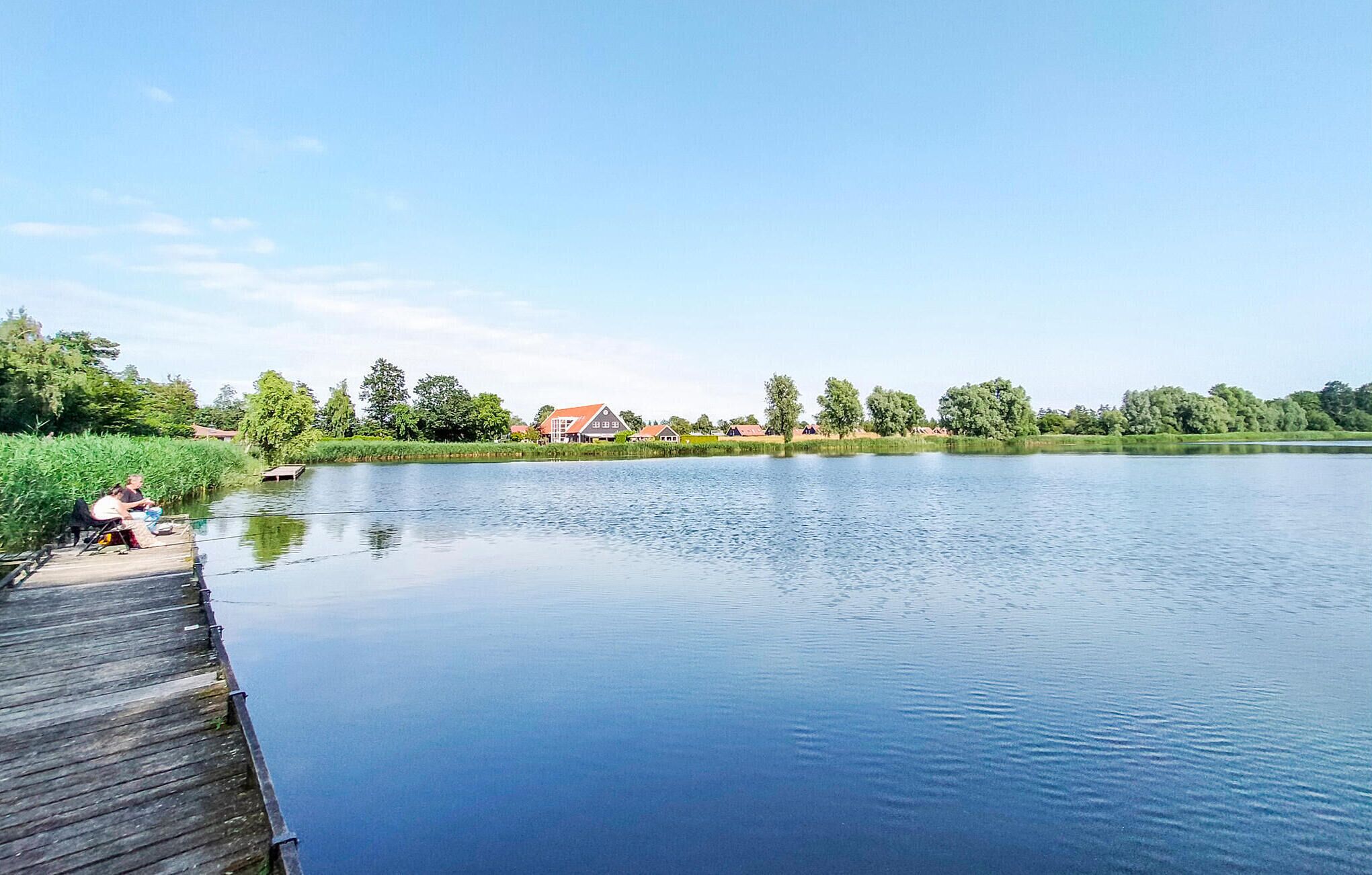 A calm lake with a wooden dock and houses in the background.