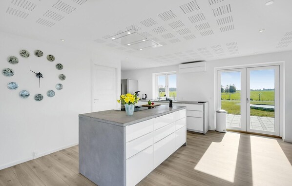 A modern kitchen with a central island, white cabinetry, and a view of a green field through large sliding doors.