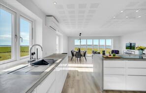 A modern kitchen with a large island, a dining area with a view of the outdoors, and a flat-screen TV.