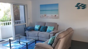 A living room with a sofa, a glass coffee table, and a painting of a beach scene. - Luxury Haven, Pool, Internet, HDTV, Gym (Palm Cove)